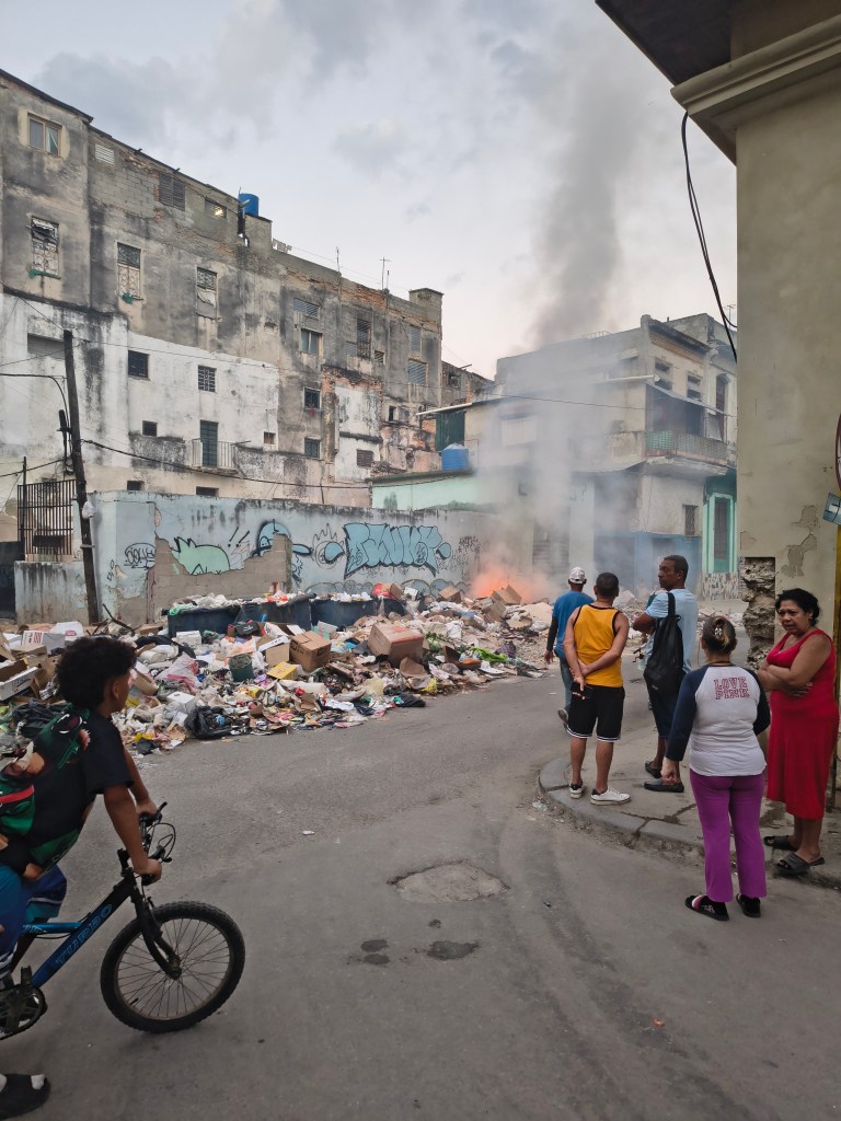 Residents watch as a garbage heap burns at a Havana street corner. With fuel shortages crippling waste collection, setting fire to accumulating trash has become a common sight across the city.